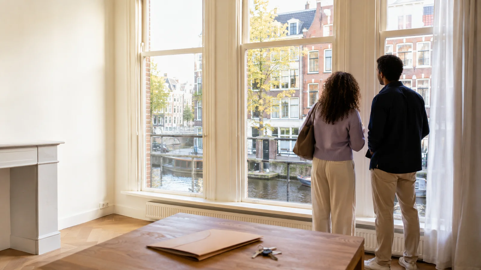 An international couple viewing Amsterdam canal homes from a bright apartment balcony